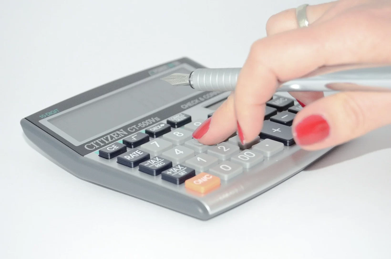 The image with a white background shows a calculator and the hand of a woman working on it.